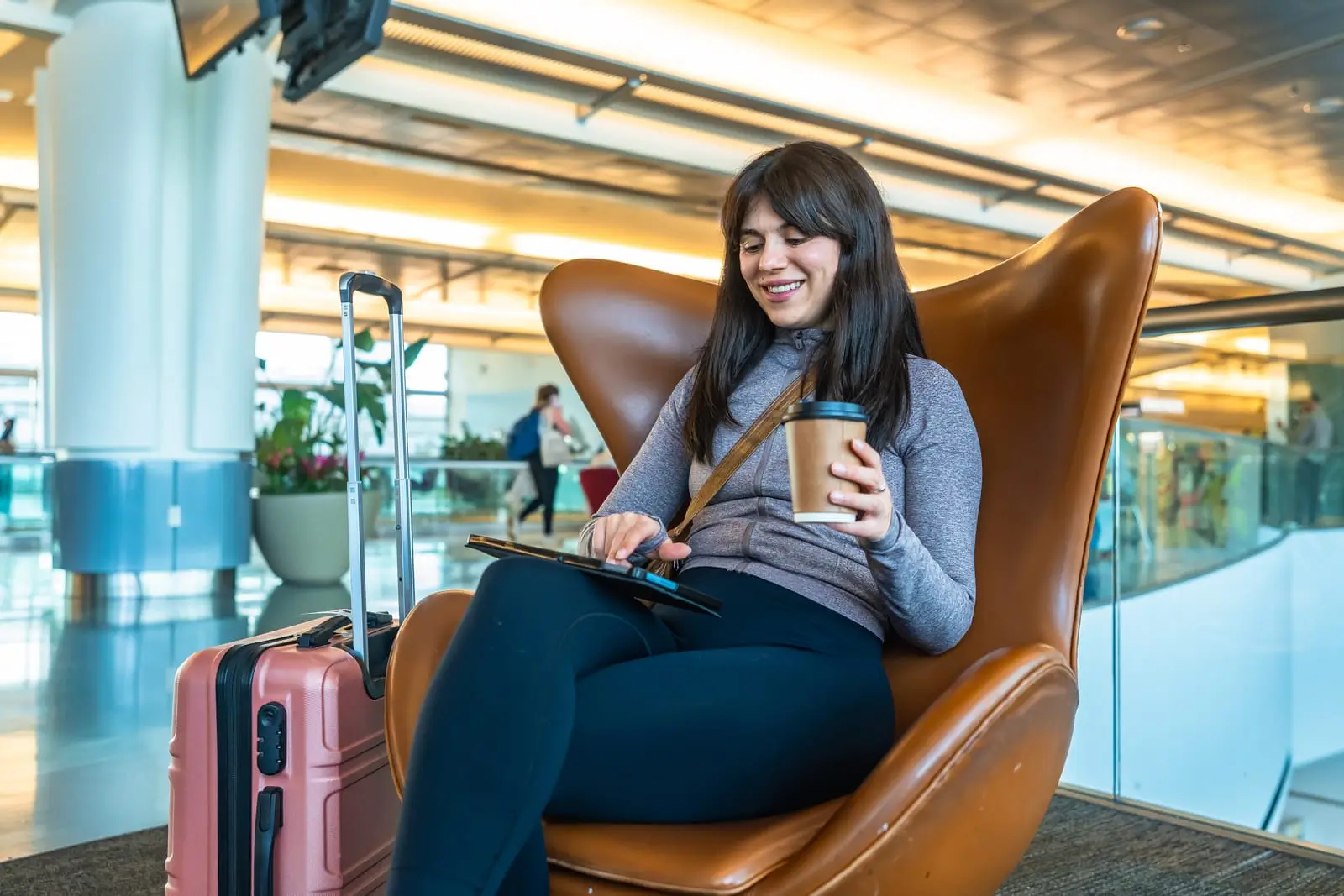 kvinne reiser avslappende med kaffe og nettbrett i flyplassloungen