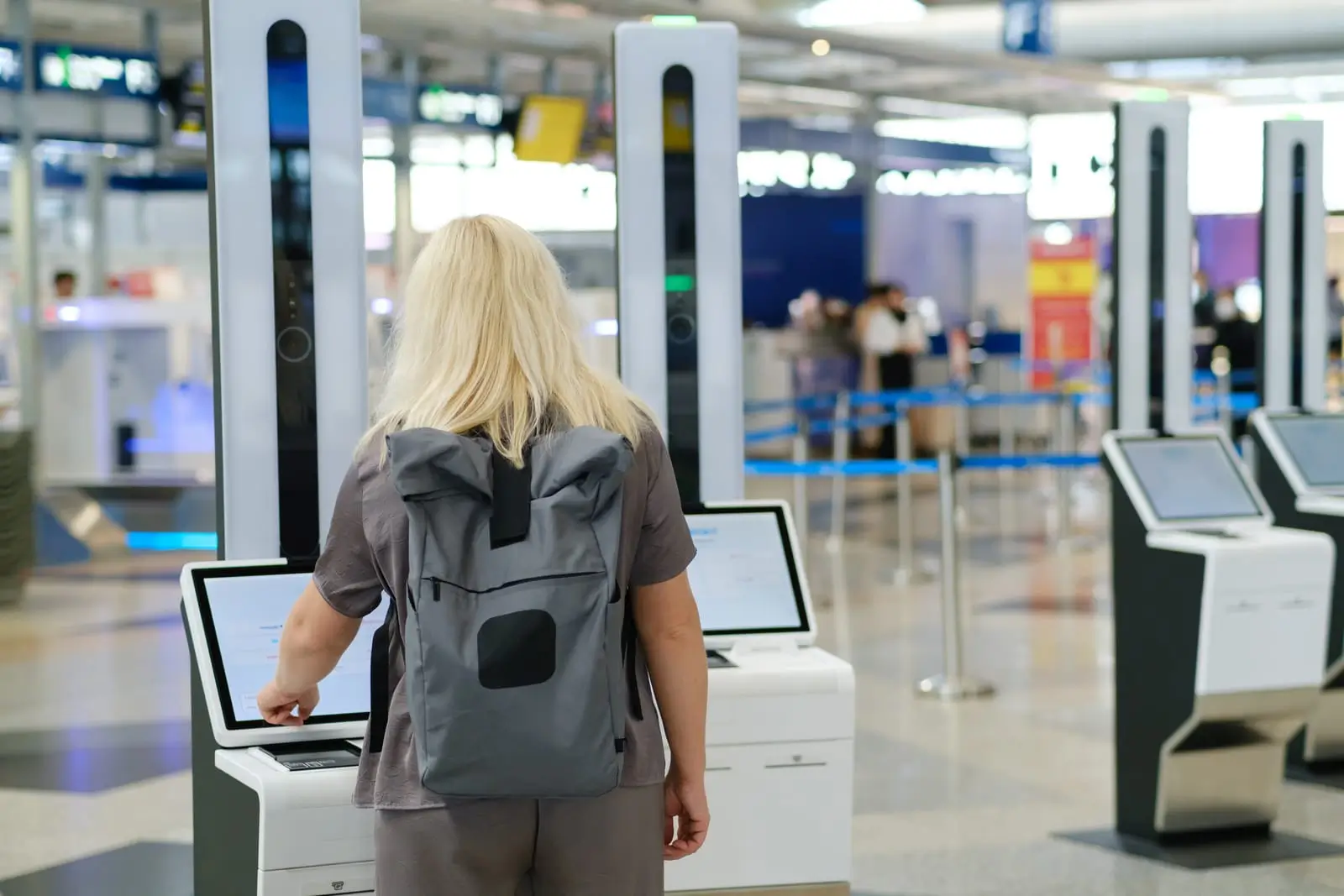 Kvinne sjekker inn på en flyplass ved bruk selvbetjeningskiosk