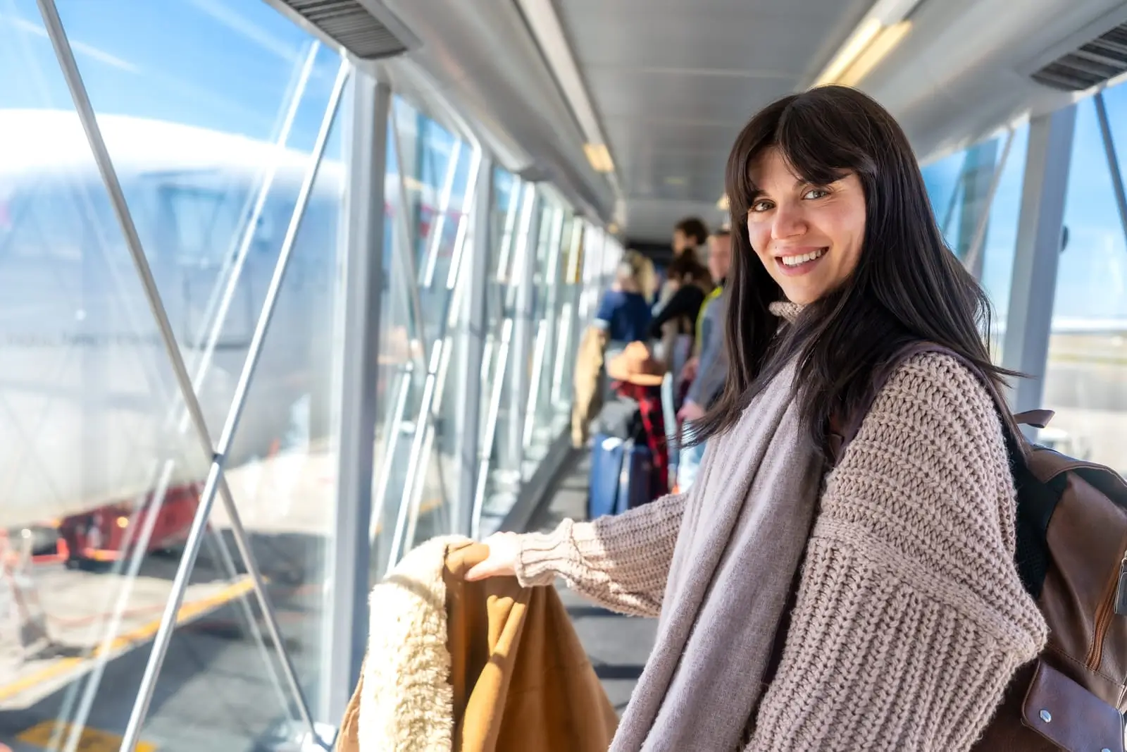 vrouw die glimlacht terwijl ze aan boord van een vliegtuig stapt dat aan een passagiersbrug wordt gekoppeld
