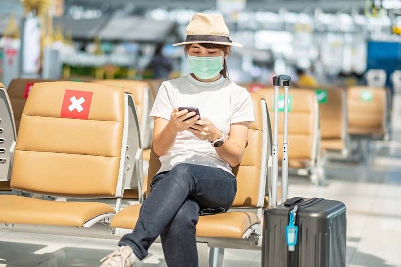 Pasajera joven con sombrero en el aeropuerto mira el móvil por los retrasos de tuifly