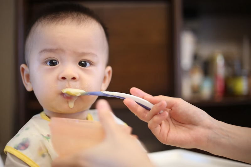 Bimbo asiatico che mangia la pappa con cucchiaino