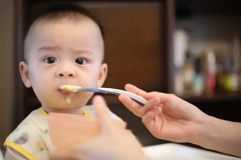 Bimbo asiatico che mangia la pappa con cucchiaino