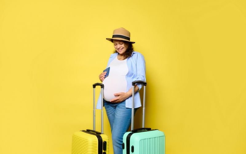 Genrebild över en gravid kvinna med resväskor och pass i handen
