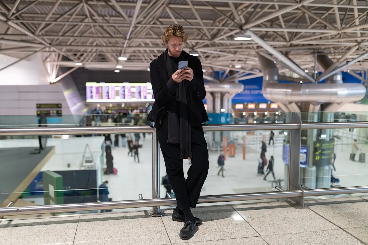 Uomo all'aeroporto di Malpensa che controlla lo stato del suo volo sul cellulare