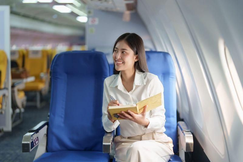 Genrebild över en kvinna sittandes på ett flygplan med ett anteckningsblock i handen