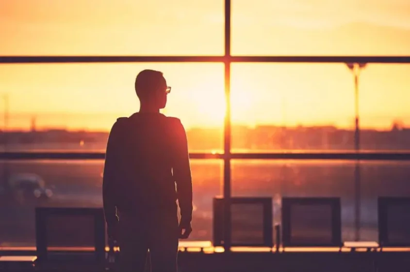 Genrebild över en resenär ståendes i flyghallen under solnedgången.