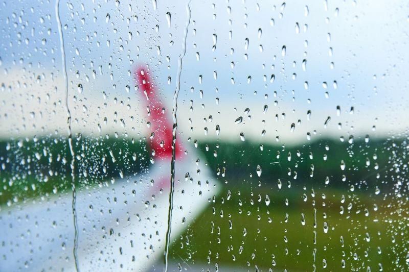 Genrebild över ett regnigt flygplansfönster och en vinge i bakgrunden