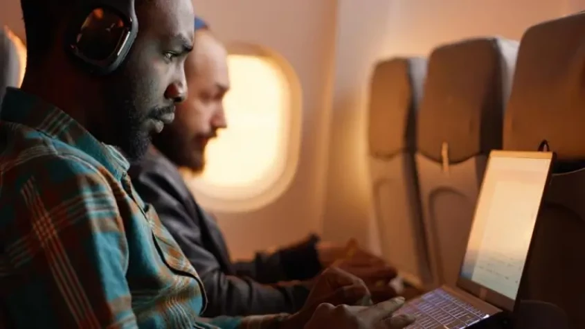 Genrebild över två resenärer där ena arbetar på sin laptop, respektive lyssnar på musik