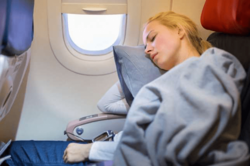 Ragazza che dorme con cuscino su un aereo in volo