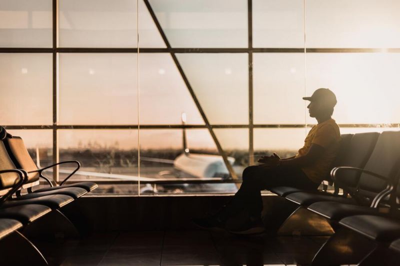 Uomo con cappellino seduto davanti alla vetrata dell’aeroporto