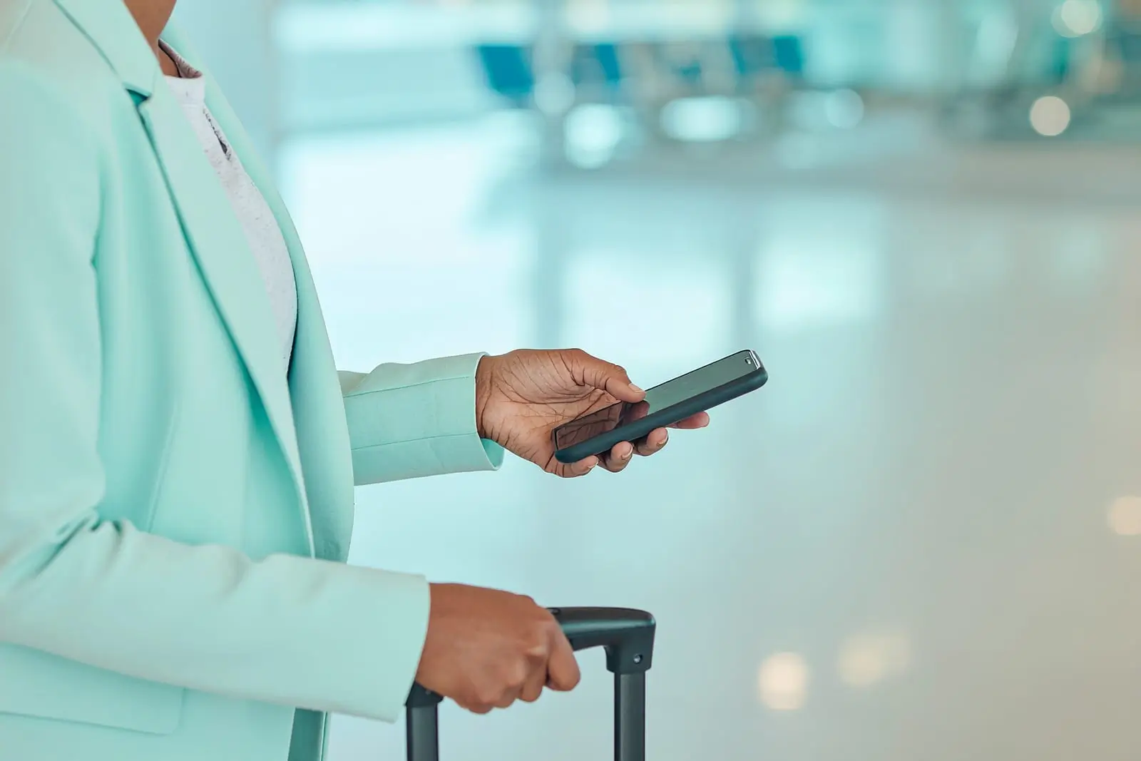 une voyageuse avec une valise &agrave; roulettes qui regarde son t&eacute;l&eacute;phone