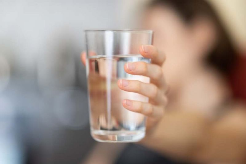 A close-up of a young woman's hand holding up a glass of water