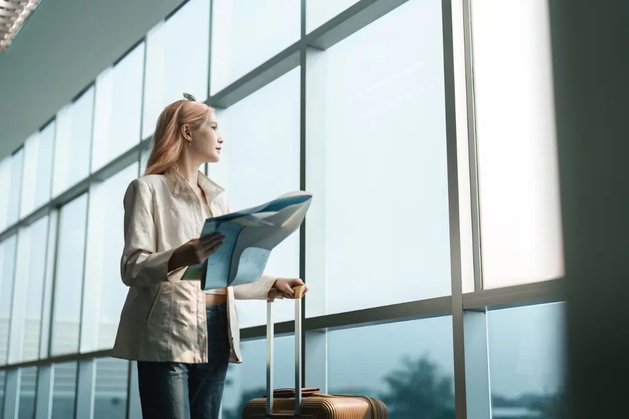 una mujer joven de pie en el aeropuerto cerca de la maleta y la lectura de mapa