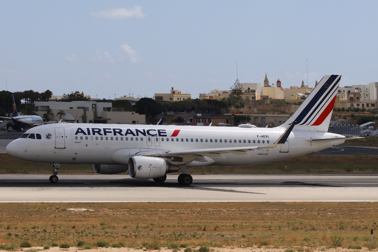 A white Air France plane taxiing on the runway with buildings in the distance