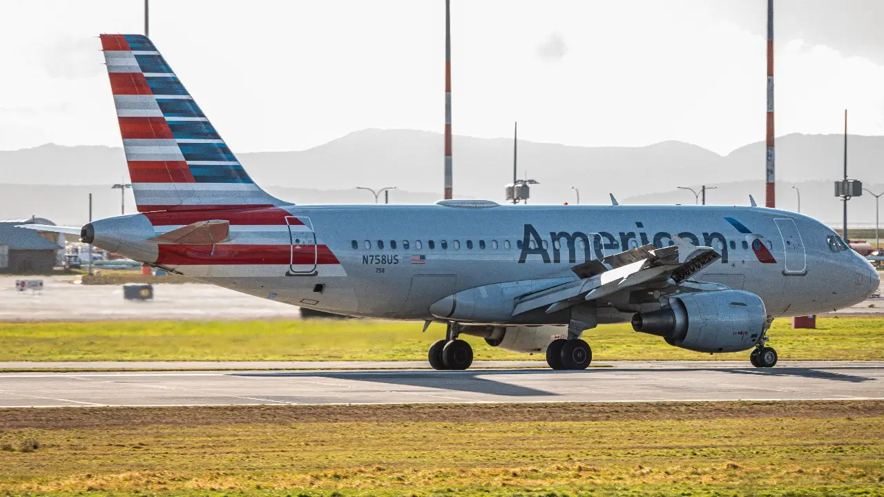 A delayed American Airlines plane finally lands at an airport with yellow grass and haze in the distance