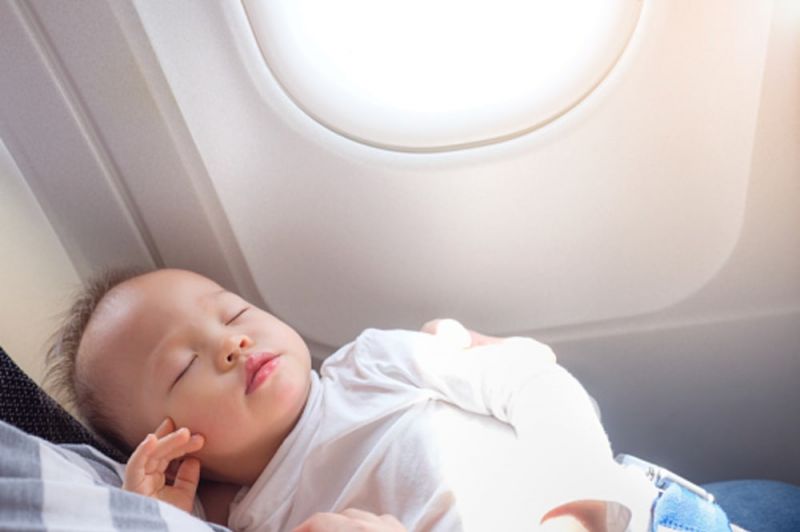 A baby sleeping on the plane next to the window