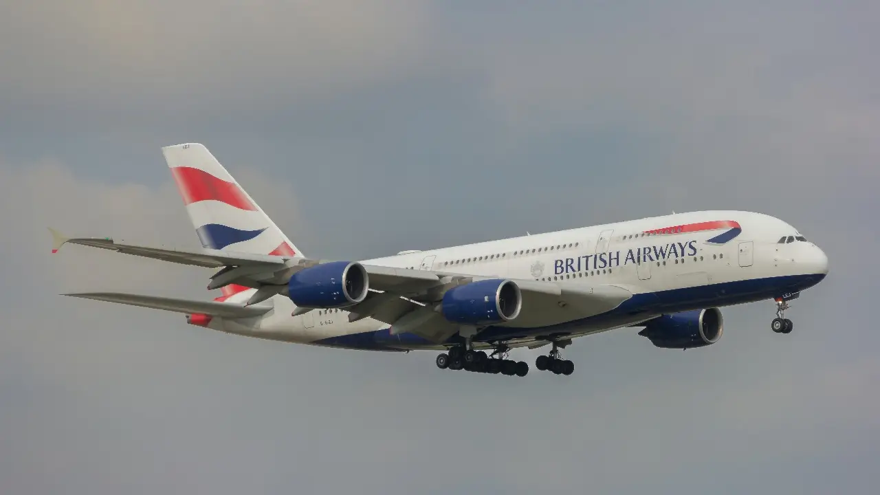 A British Airways white, red, and blue plane flying through a cloudy sky