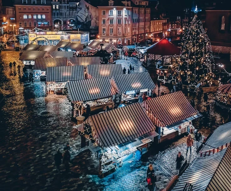 Christmas market stalls and a lit Christmas tree in an old town square at night