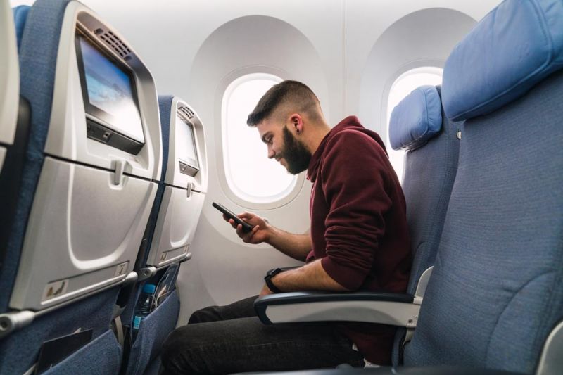 Hombre comprobando con su móvil si se puede usar el WiFi en el avión
