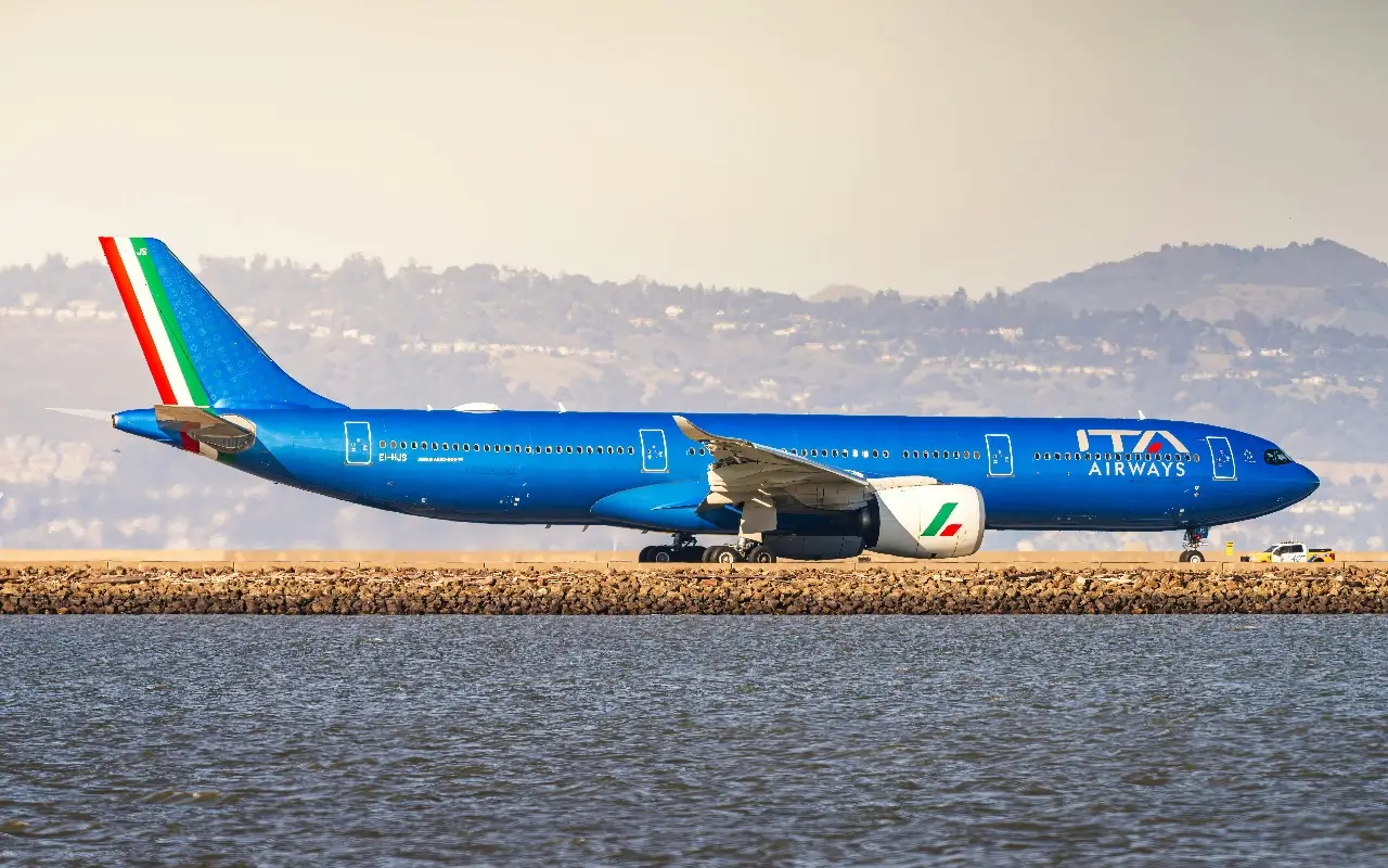 A bright blue ITA Airways plane on the runway surrounded by water at San Francisco Airport