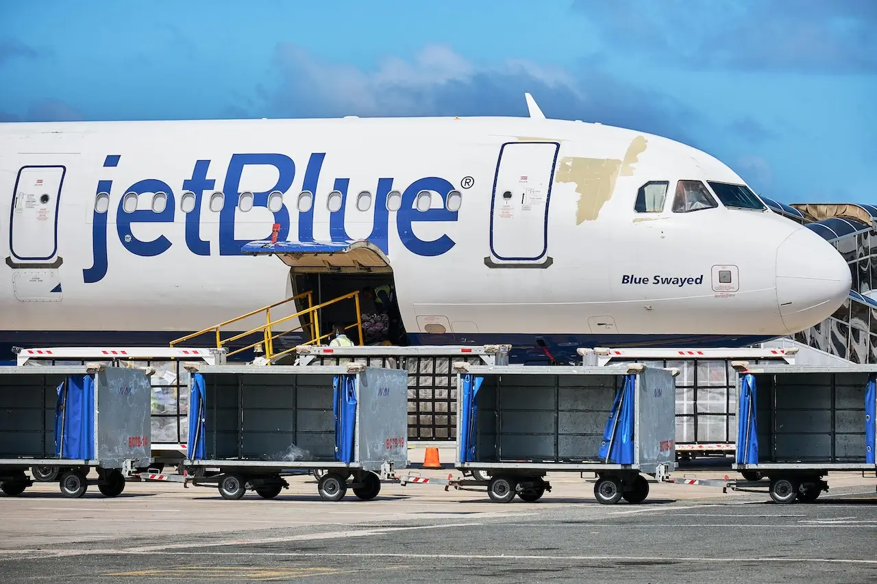 A jetBlue plane parked at the gate and offloading baggage