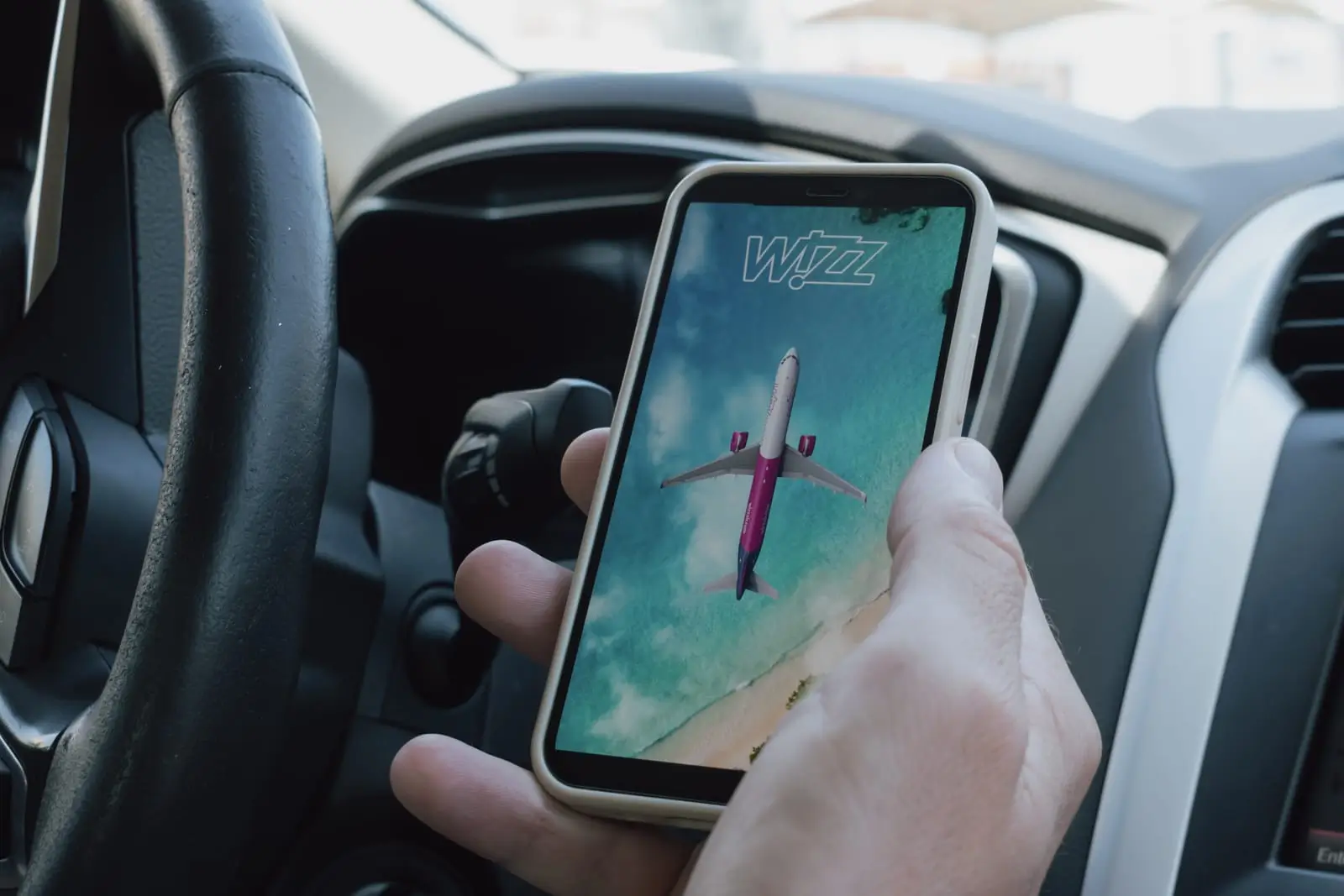 m&acirc;na unui bărbat &icirc;ntr-o mașină, țin&acirc;nd un telefon pe care este deschisă aplicația companiei aeriene Wizz Air