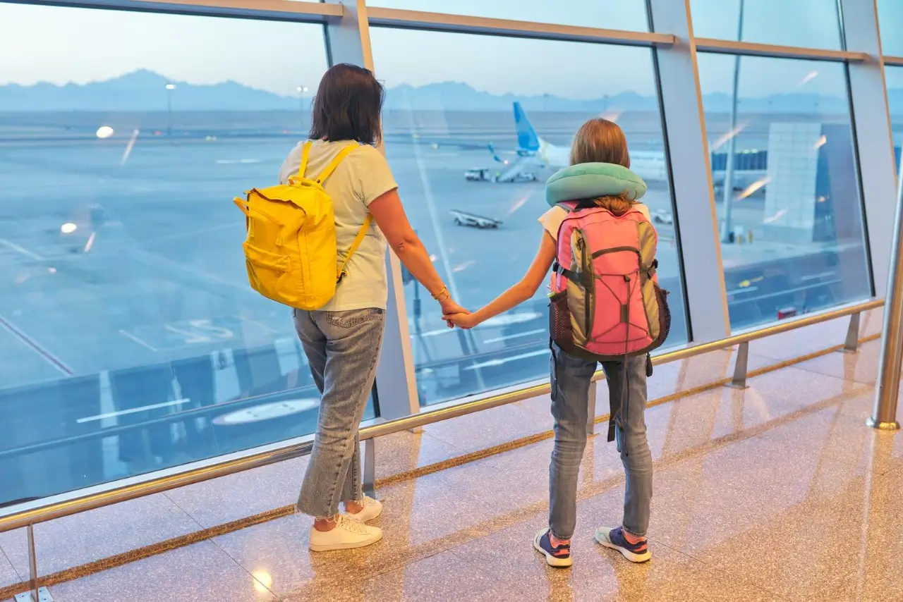 madre e hija mirando aviones en ventana panorámica