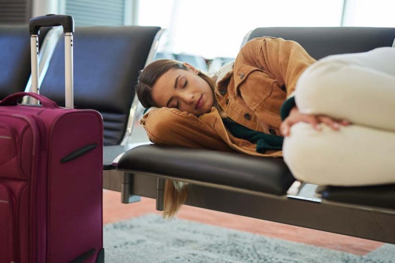 Mujer joven con maletas duerme en sala de espera de aeropuerto por retraso de vuelos de Aerolíneas Argentinas