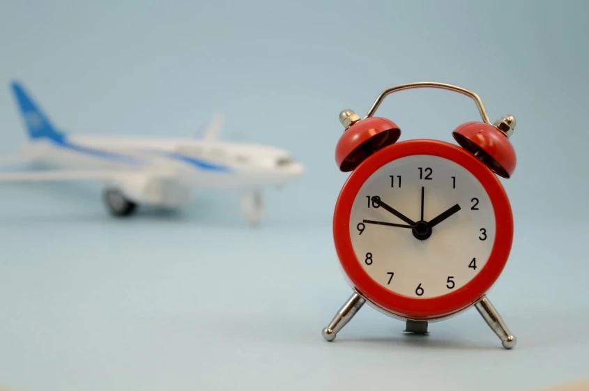 Primer plano de un reloj rojo con un avi&oacute;n de fondo