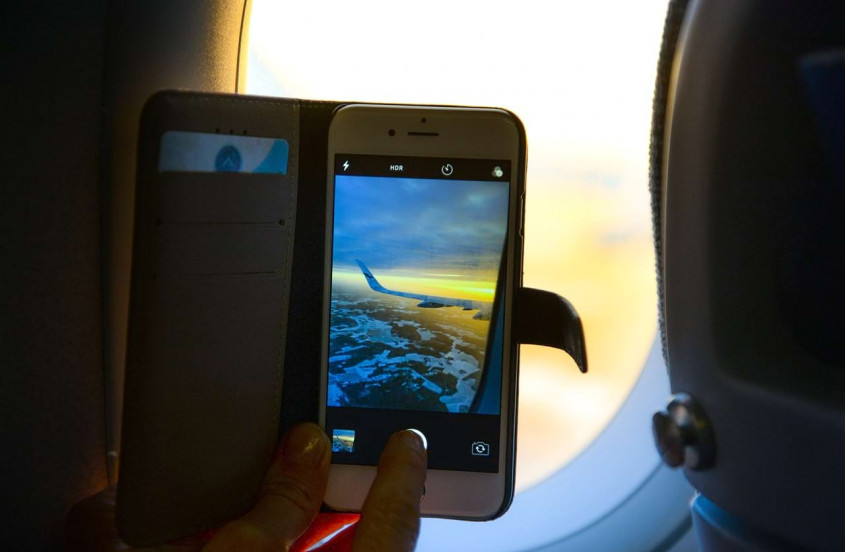 Genrebild över en resenär som fotar vingen på ett flygplan med sin mobiltelefon
