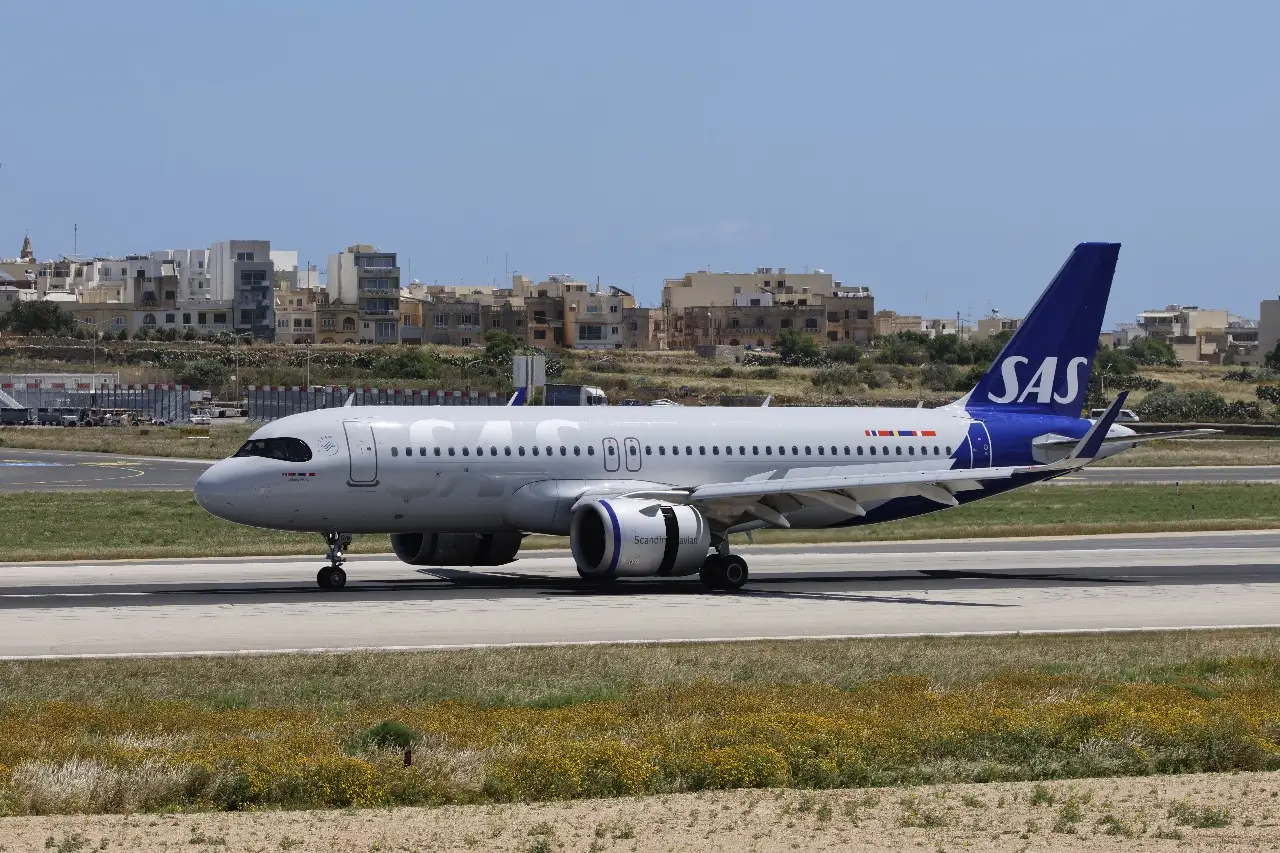 A white and blue SAS plane on the tarmac with buildings in the distance on a sunny day
