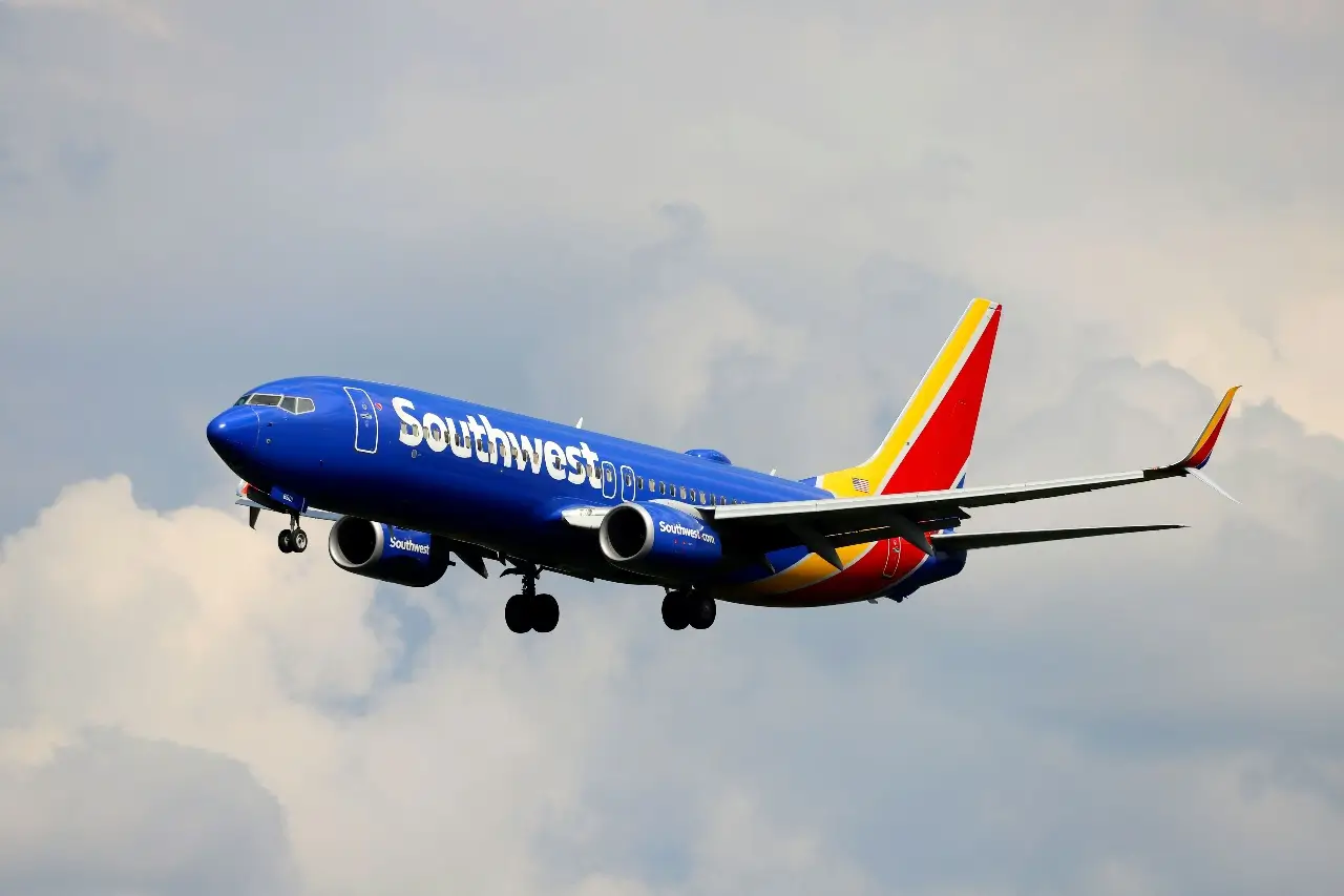 A blue, red, and yellow Southwest plane flying in a cloudy sky