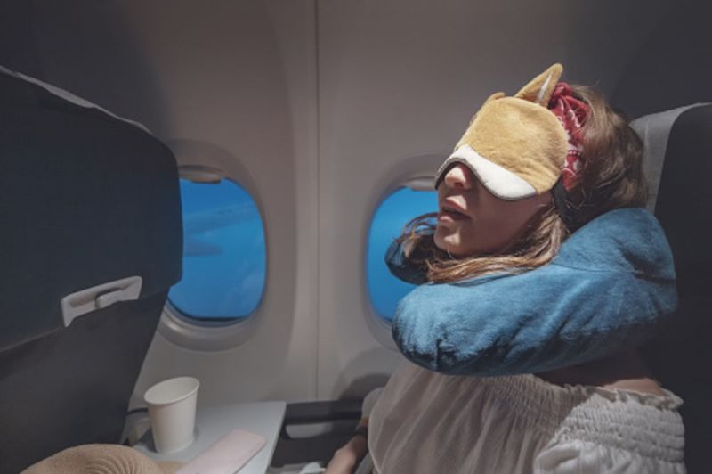 O femeie care doarme în avion cu mască de somn și pernă de călătorie