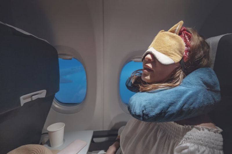 A young woman is sleeping on the plane with her sleeping mask and a neck pillow on