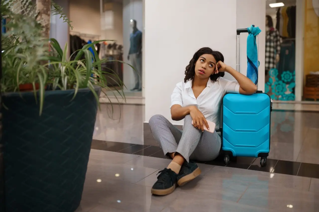femme avec valise assise par terre &agrave; l'a&eacute;roport