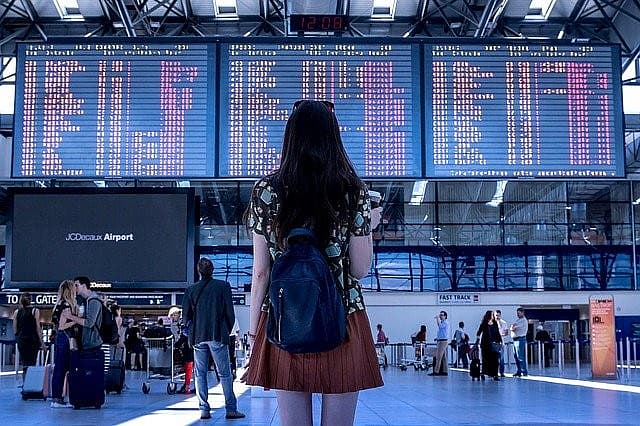Frau blickt auf Abflugtafel am Flughafen