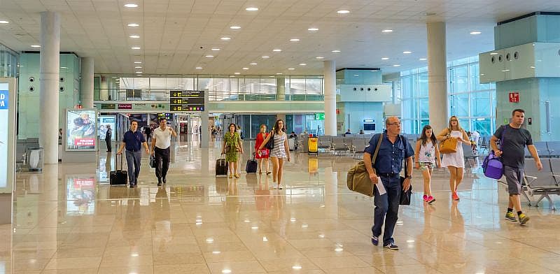 Pasajeros con maletas caminan por los pasillos iluminados del aeropuerto Barcelona-El Prat.