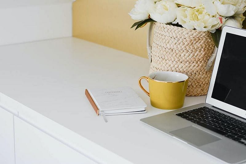 Scrivania bianca con agenda, tazza, fiori e computer