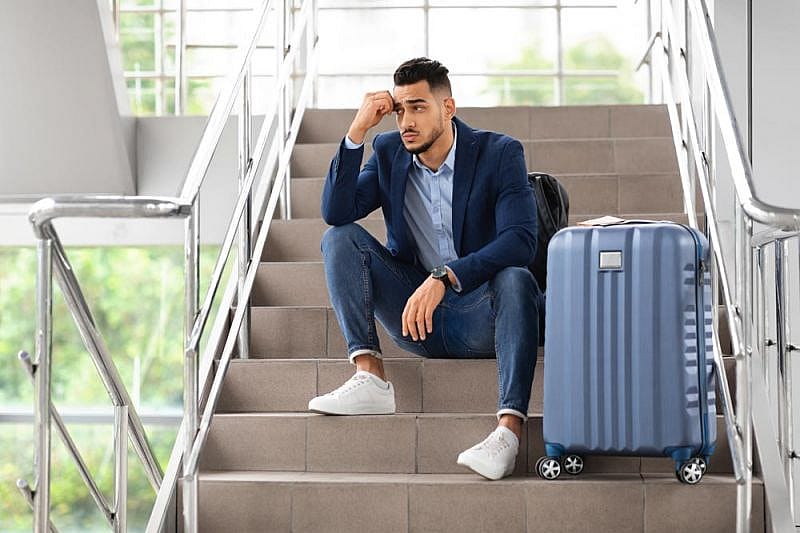 Passegero seduto sulle scale di un aeroporto in attesa del suo volo in ritardo