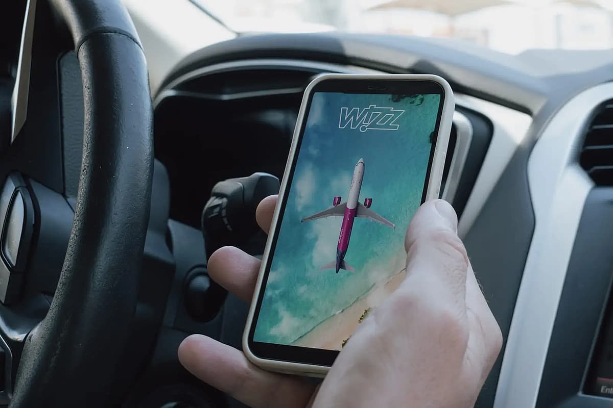 m&acirc;na unui bărbat &icirc;ntr-o mașină, țin&acirc;nd un telefon pe care este deschisă aplicația companiei aeriene Wizz Air