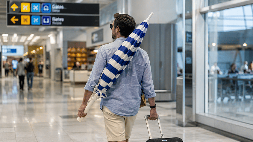 Putnik nosi sklopljeni plažni suncobran na aerodromu
